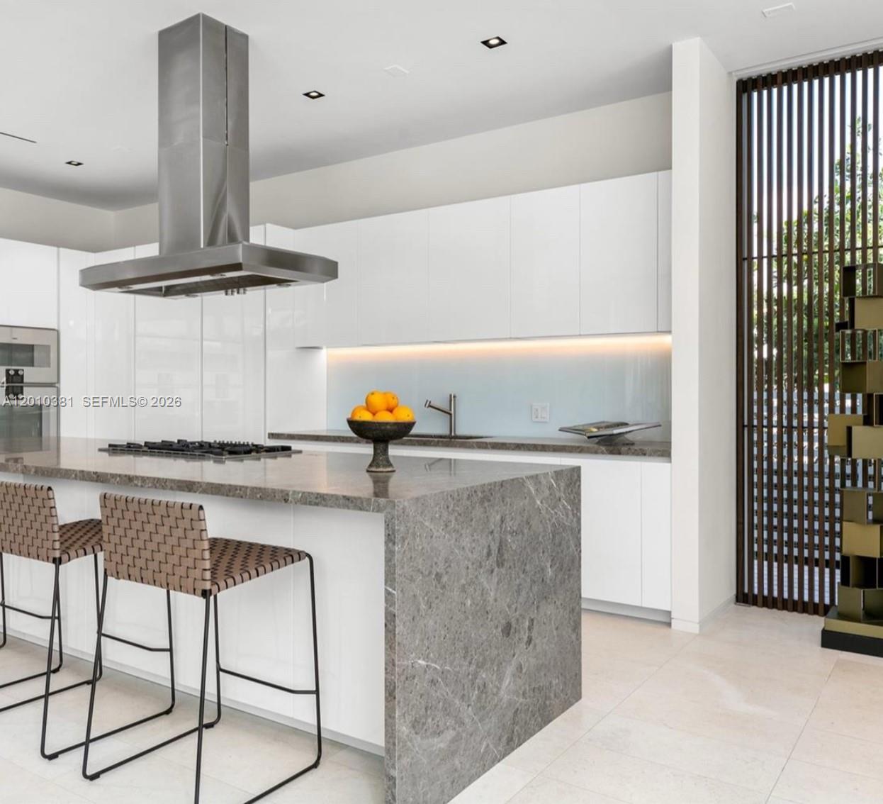 A modern kitchen features a large stone waterfall island, white cabinetry, and a stainless hood — 1081 W 48th St # N01, Miami Beach FL 33140, MIAMI BEACH, FL