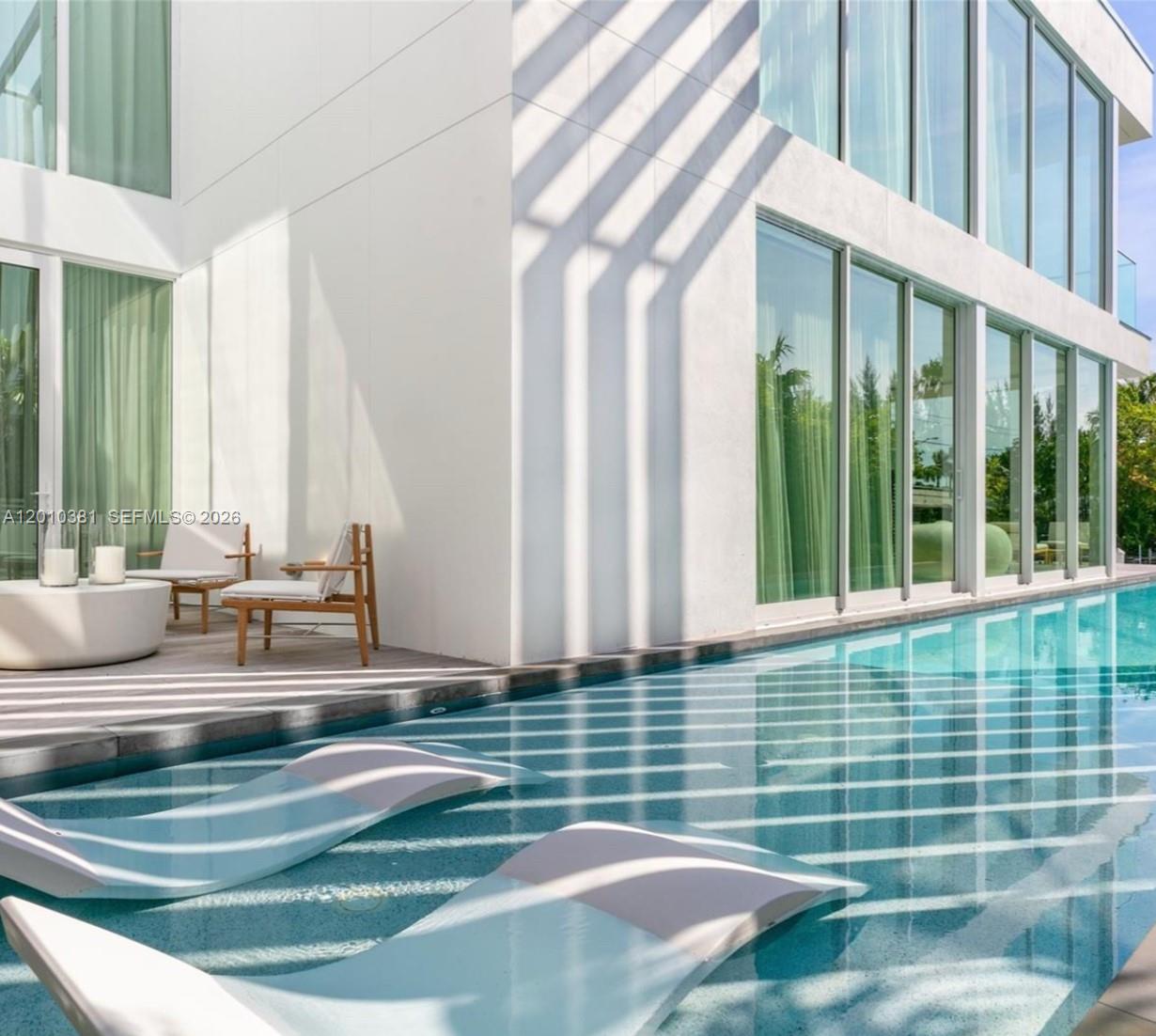 A modern white house exterior features a swimming pool with lounge chairs and large windows — 1081 W 48th St # N01, Miami Beach FL 33140, MIAMI BEACH, FL