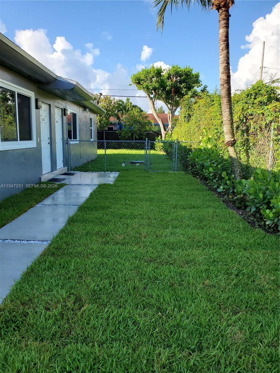 A side yard with a concrete walkway, green grass, a chain-link fence, and palm trees — 1170 NE 111th St # 1170, Miami FL 33161, MIAMI, FL