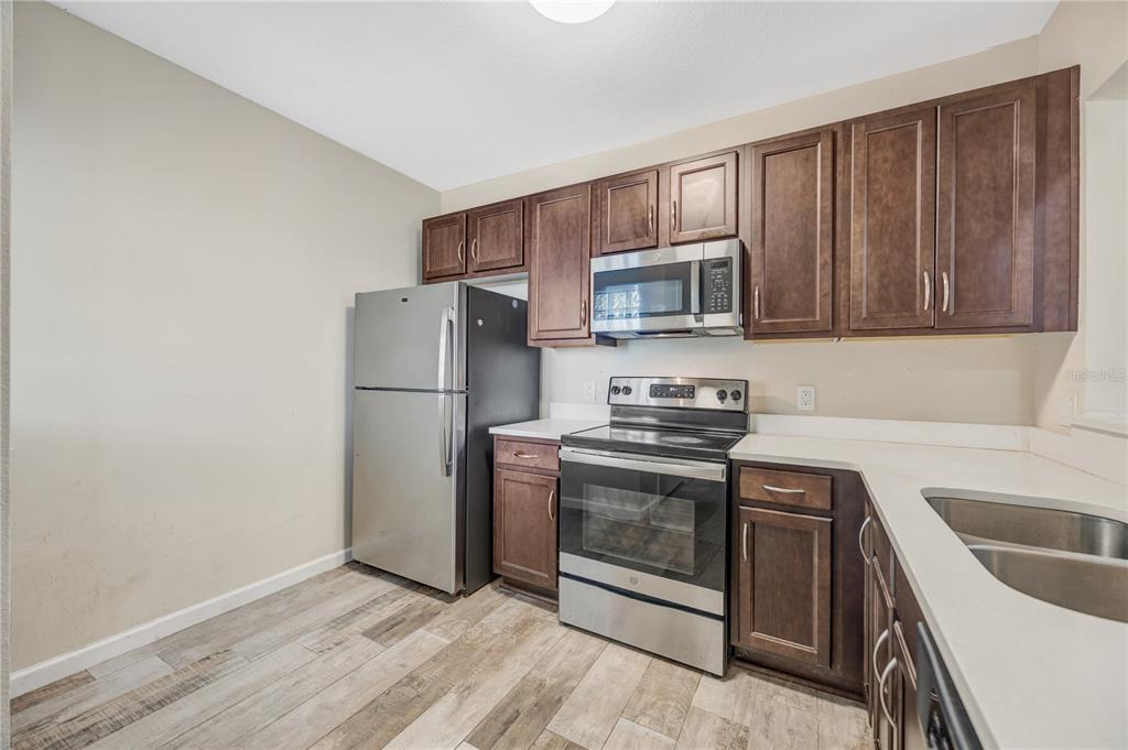 A kitchen features dark wood cabinets, stainless steel appliances, white countertops, and wood-look flooring — 1231 GODAVARI WAY E UNIT 202, WESLEY CHAPEL, FL
