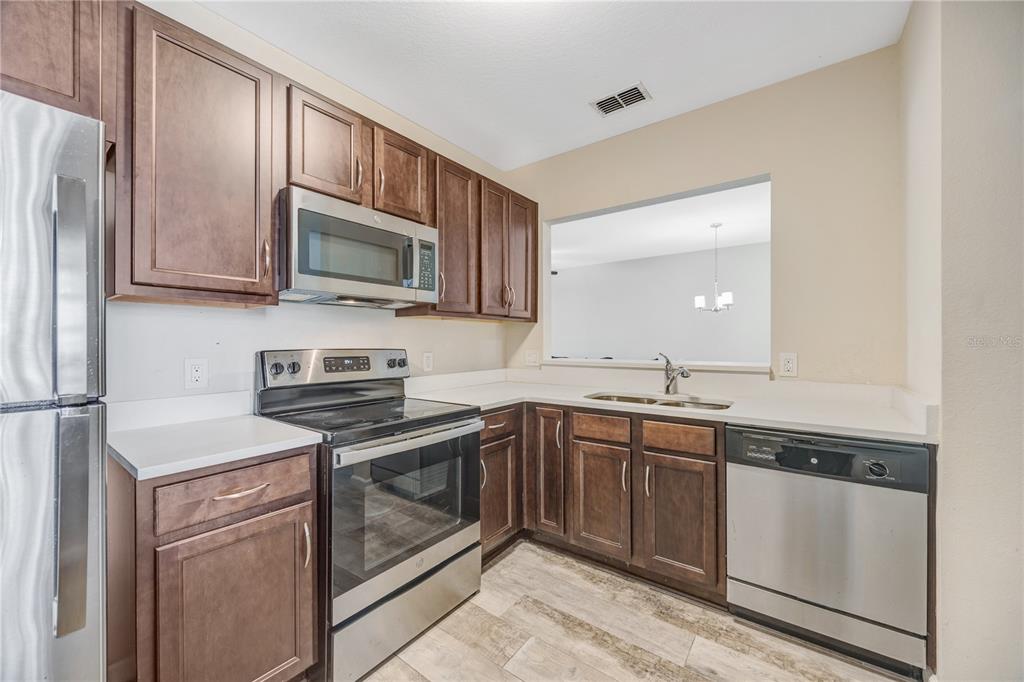 A kitchen with dark wood cabinets, stainless steel appliances, and light-colored countertops — 1231 GODAVARI WAY E UNIT 202, WESLEY CHAPEL, FL