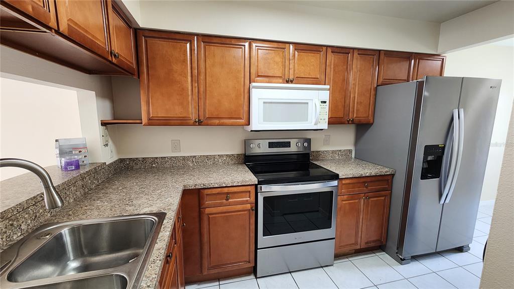 A kitchen features wood cabinets, granite countertops, stainless steel appliances, and a white microwave — 2211 MARGARITA COURT UNIT 2211, KISSIMMEE, FL