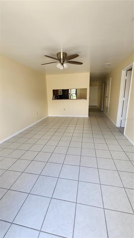 An open living area features light-colored tile flooring, a ceiling fan, and a kitchen pass-through window — 2211 MARGARITA COURT UNIT 2211, KISSIMMEE, FL