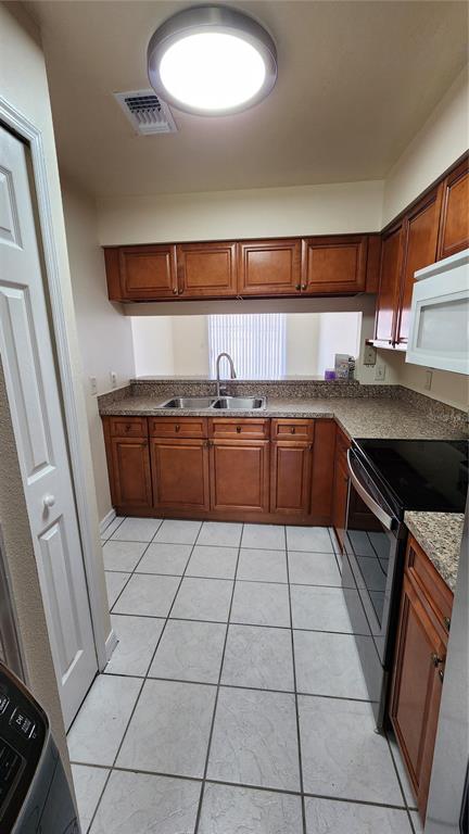 A kitchen features wood cabinets, granite countertops, a double sink, and white tile flooring — 2211 MARGARITA COURT UNIT 2211, KISSIMMEE, FL