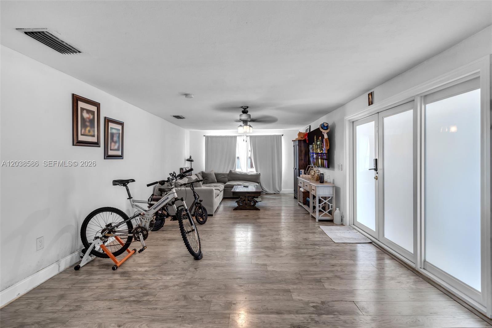 A living room features light wood-look flooring, a sectional sofa, and a stationary bicycle — 3510 SW 87th Ave, Miami FL 33165, MIAMI, FL
