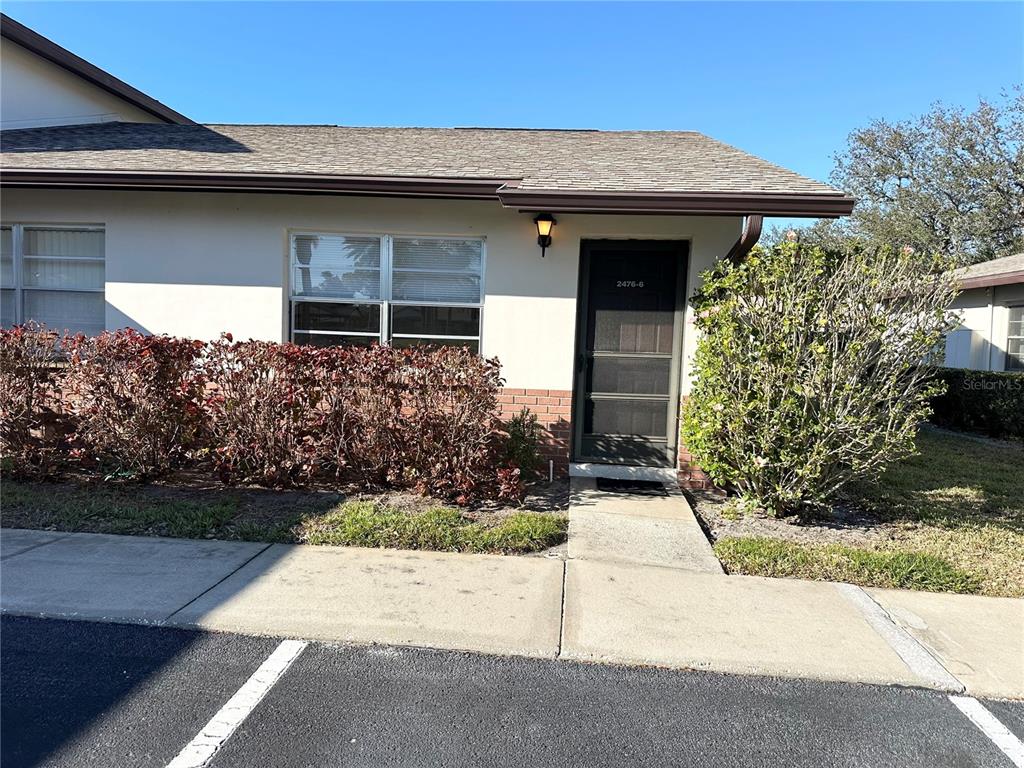 A single-story building exterior features a brown shingled roof, white walls, and a screen door — 2476 ENTERPRISE ROAD UNIT 6, CLEARWATER, FL
