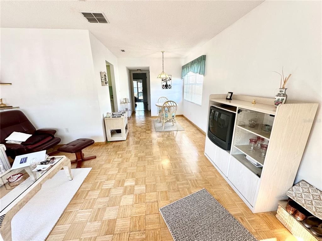 A living and dining area features parquet wood flooring, a television console, and white walls — 2476 ENTERPRISE ROAD UNIT 6, CLEARWATER, FL