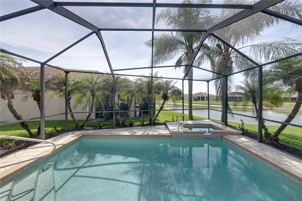 A screened-in swimming pool and spa overlook a canal with palm trees in the background — 4017 DUNMORE DRIVE, LAKE WALES, FL