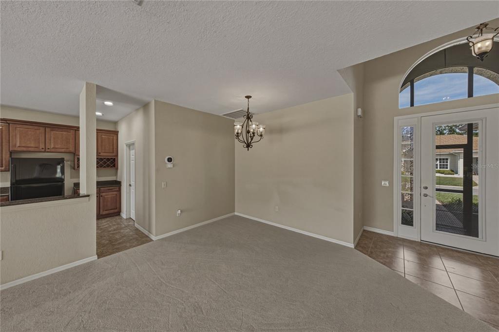 A dining area with carpeted flooring, a chandelier, and an adjacent kitchen with wood cabinets — 4017 DUNMORE DRIVE, LAKE WALES, FL