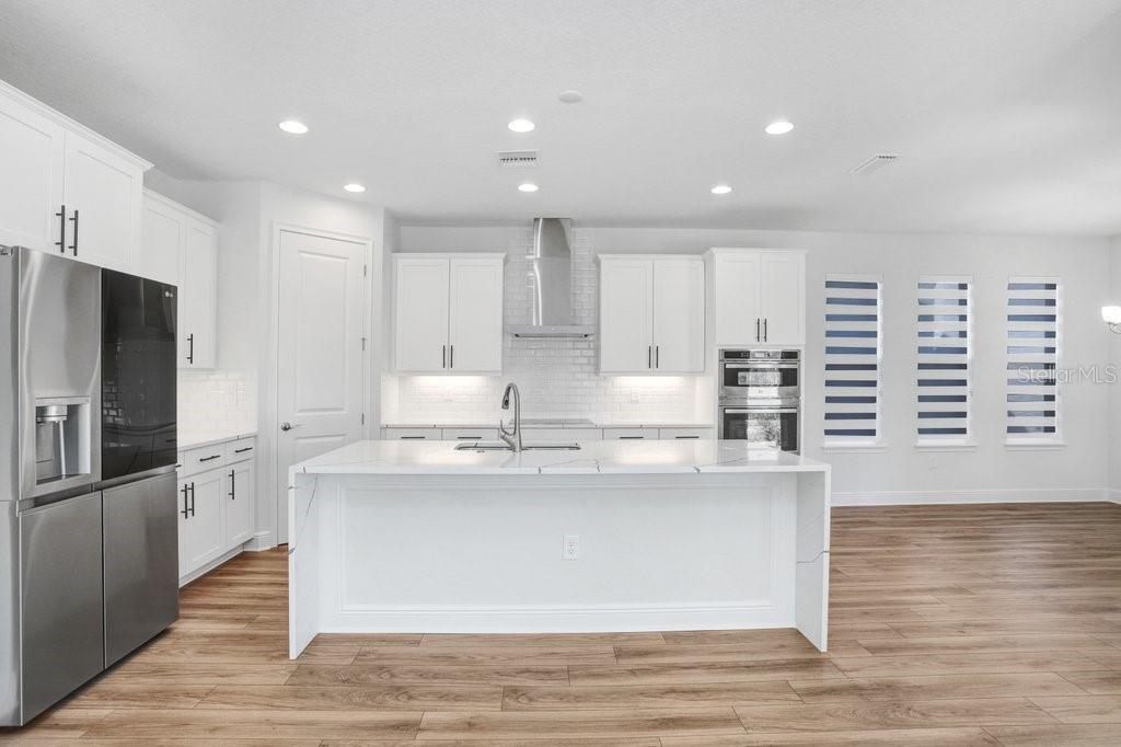 A modern kitchen features white cabinetry, a large marble-topped island, and stainless steel appliances — 28793 SWEET PERSIMMON DRIVE, WESLEY CHAPEL, FL