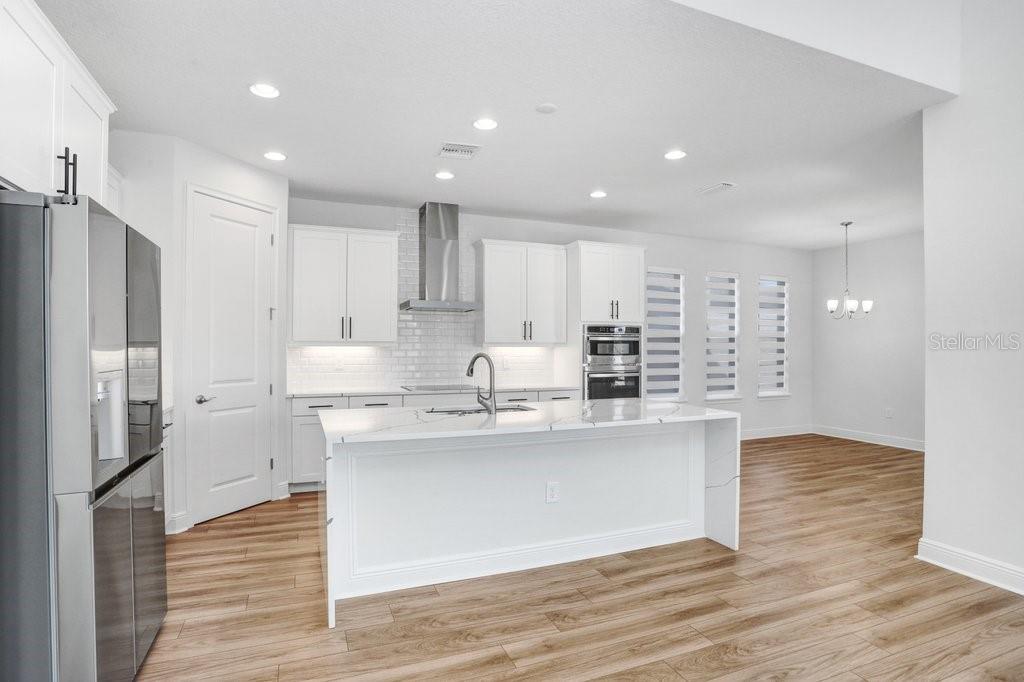 A modern kitchen features white cabinetry, a large marble-topped island, and light wood flooring — 28793 SWEET PERSIMMON DRIVE, WESLEY CHAPEL, FL