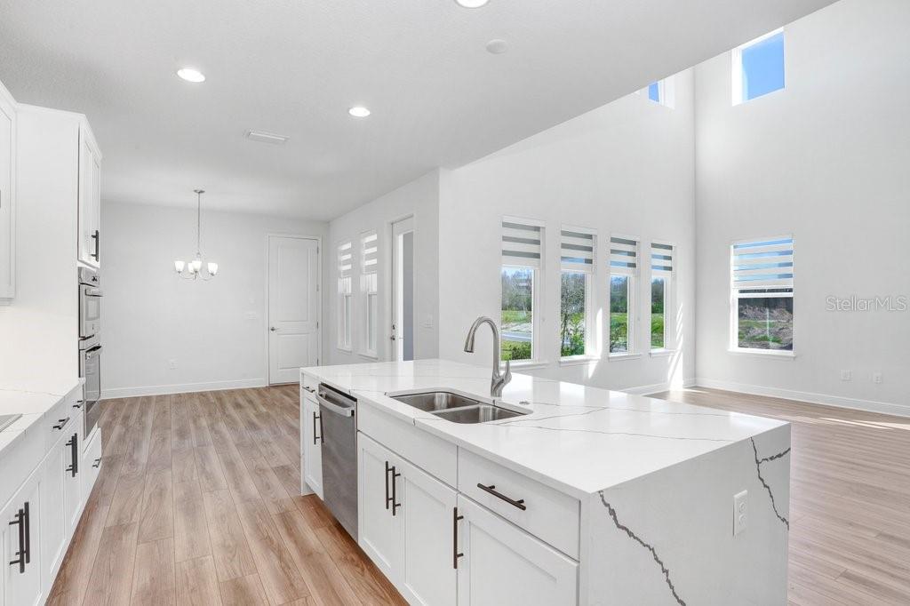 A modern kitchen features white cabinetry, a quartz island with a sink, and light flooring — 28793 SWEET PERSIMMON DRIVE, WESLEY CHAPEL, FL