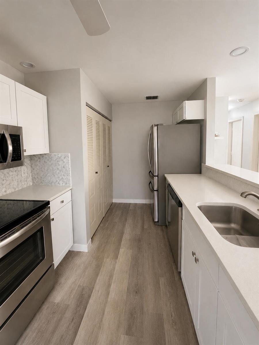 A galley kitchen features white cabinets, stainless steel appliances, and light wood-look flooring — 6069 La Palma Lane, Delray Beach FL 33484, DELRAY BEACH, FL