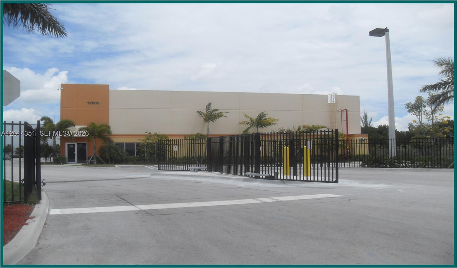 A commercial warehouse building with a gated entrance and palm trees under a cloudy sky — 12601 NW 115th Ave # 103, Medley FL 33178, MEDLEY, FL
