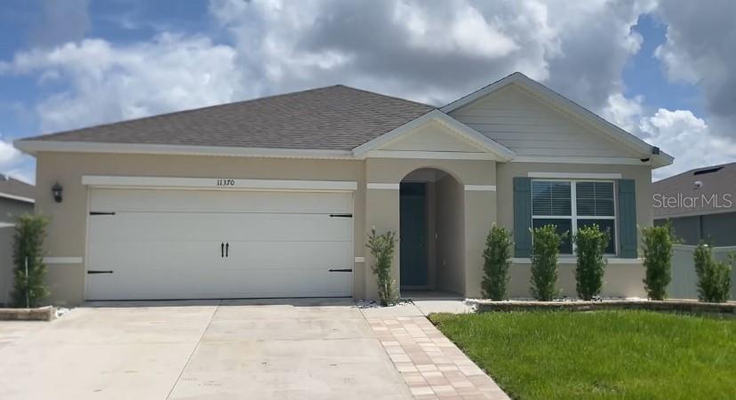 A single-story house with a beige stucco exterior, a two-car garage, and a paved walkway — 11370 AMBER RIDGE DRIVE, ZELLWOOD, FL