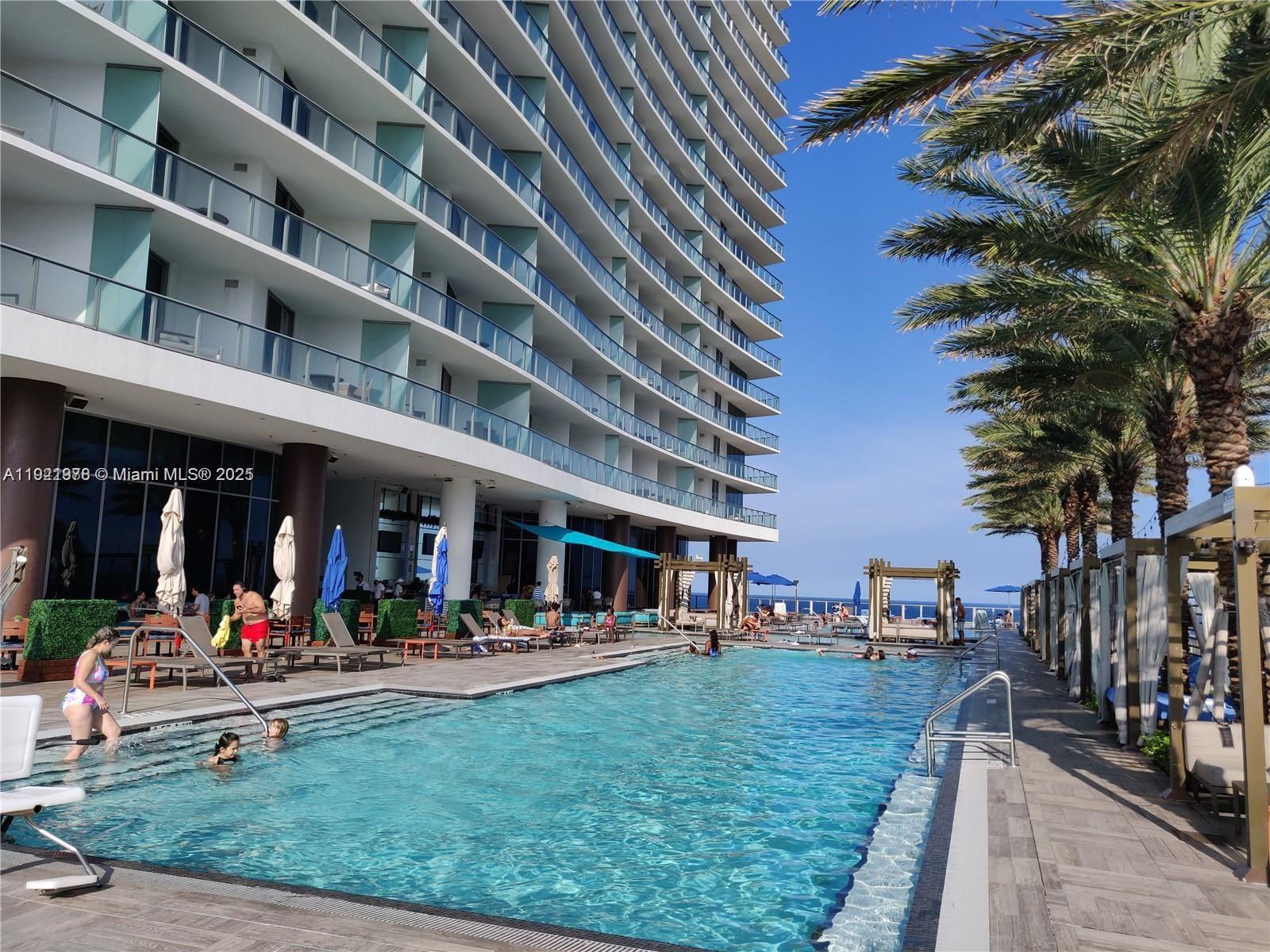 A multi-story hotel building overlooks a swimming pool with lounge chairs and palm trees — 4111 S Ocean Dr # 1506, Hollywood FL 33019, HOLLYWOOD, FL