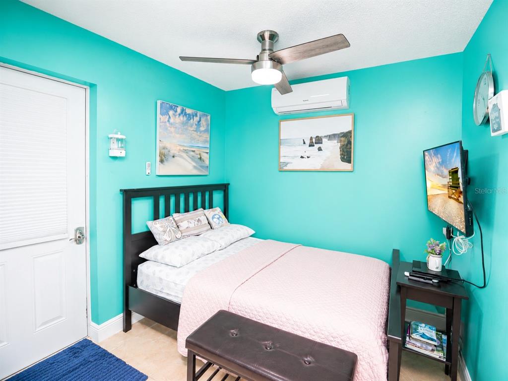 A bedroom with turquoise walls, a black bed frame, a ceiling fan, and a wall-mounted television — 111 CUAUTLA WAY UNIT 2, KISSIMMEE, FL