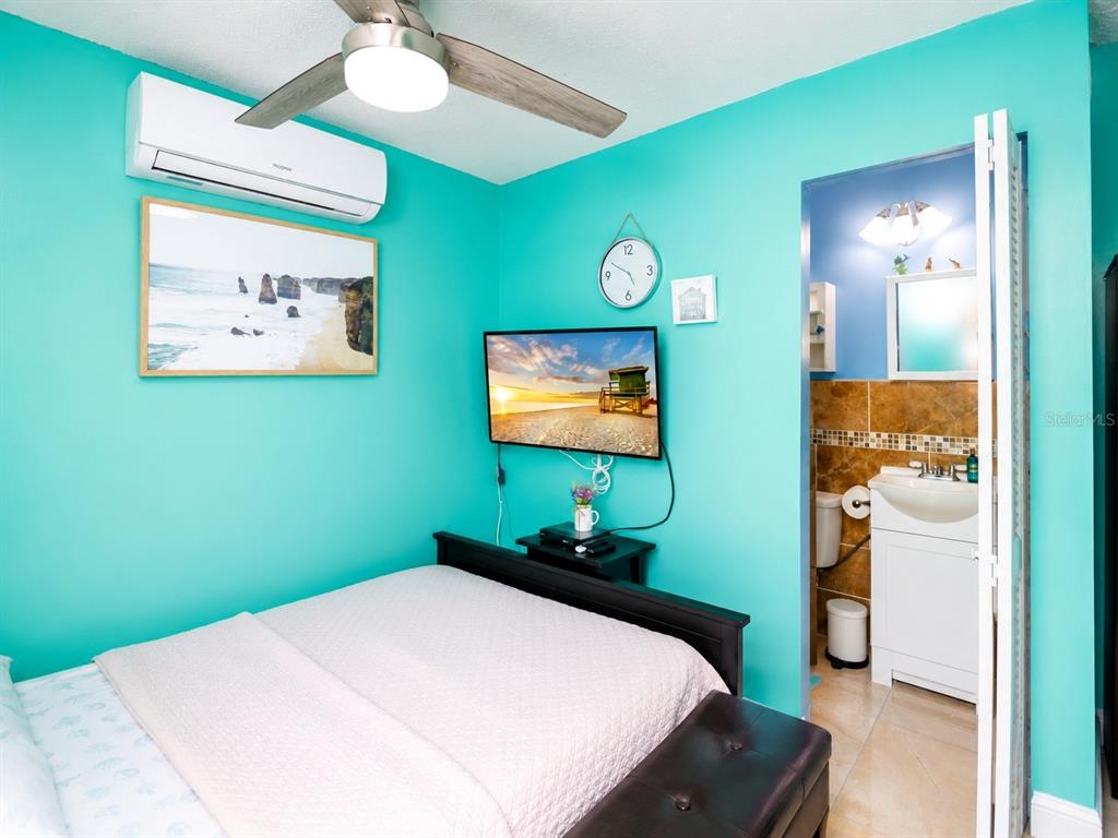 A bedroom with turquoise walls, a ceiling fan, a wall-mounted television, and an attached bathroom — 111 CUAUTLA WAY UNIT 2, KISSIMMEE, FL