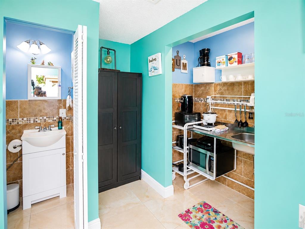 A bathroom with a pedestal sink sits next to a small kitchenette with metal shelving — 111 CUAUTLA WAY UNIT 2, KISSIMMEE, FL
