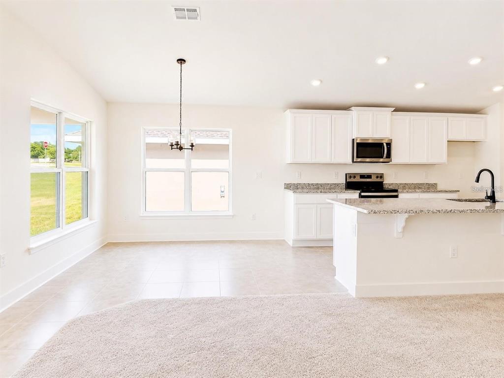 A bright kitchen and dining area features white cabinets, granite countertops, and tile flooring — 1671 ANN ROSE WAY, LEESBURG, FL