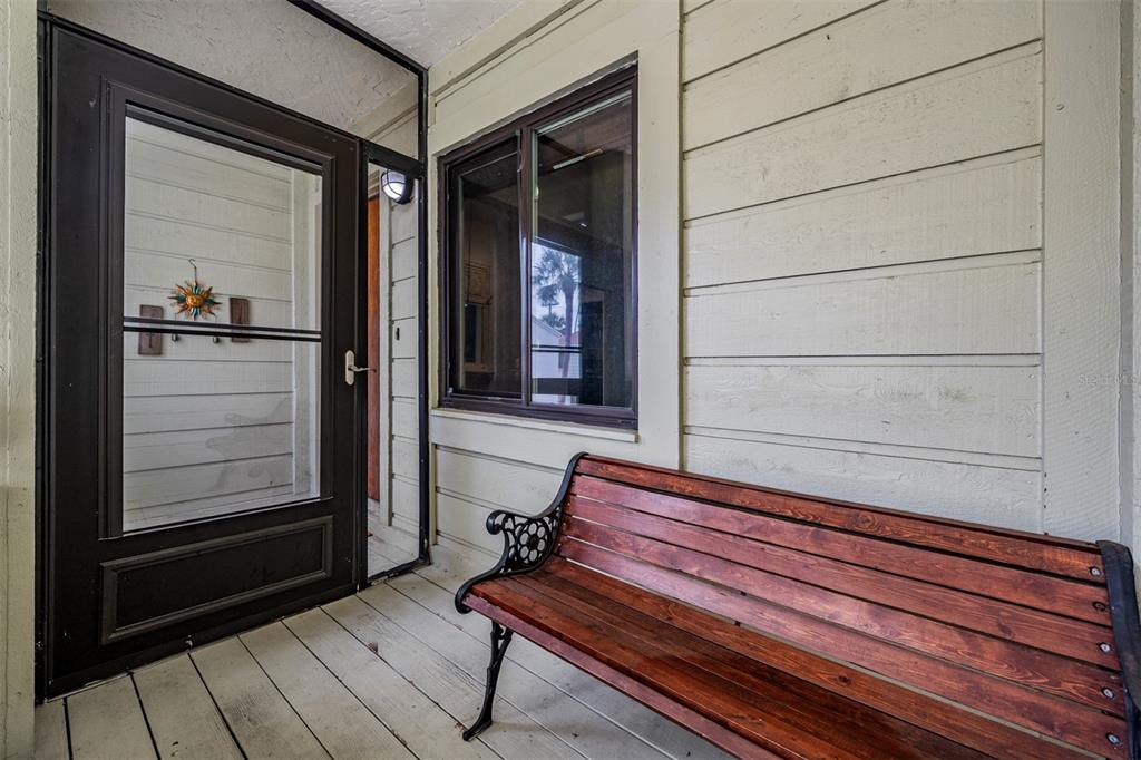 A wooden bench sits on a covered porch next to a window and a door — 637 DRAKE LANE N, DUNEDIN, FL