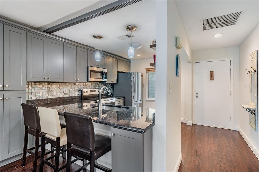 A kitchen with gray cabinets, granite countertops, and a breakfast bar with three stools — 637 DRAKE LANE N, DUNEDIN, FL