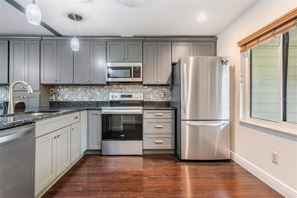 A kitchen features gray cabinets, stainless steel appliances, dark countertops, and dark wood flooring — 637 DRAKE LANE N, DUNEDIN, FL