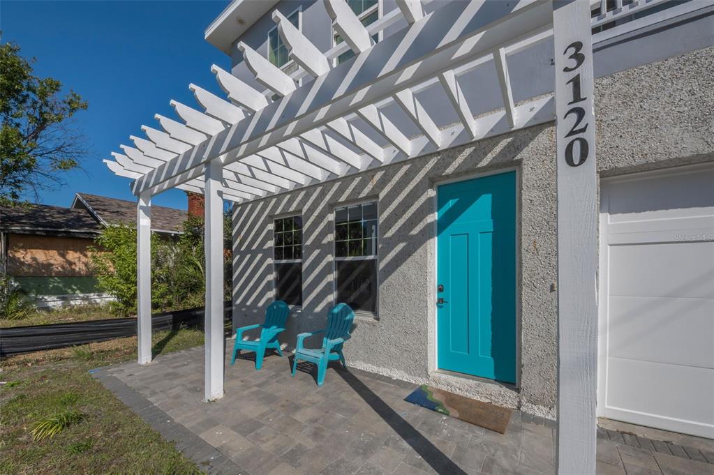 A white pergola covers a paved patio with two blue chairs and a teal door — 3120 CLINTON STREET S, GULFPORT, FL