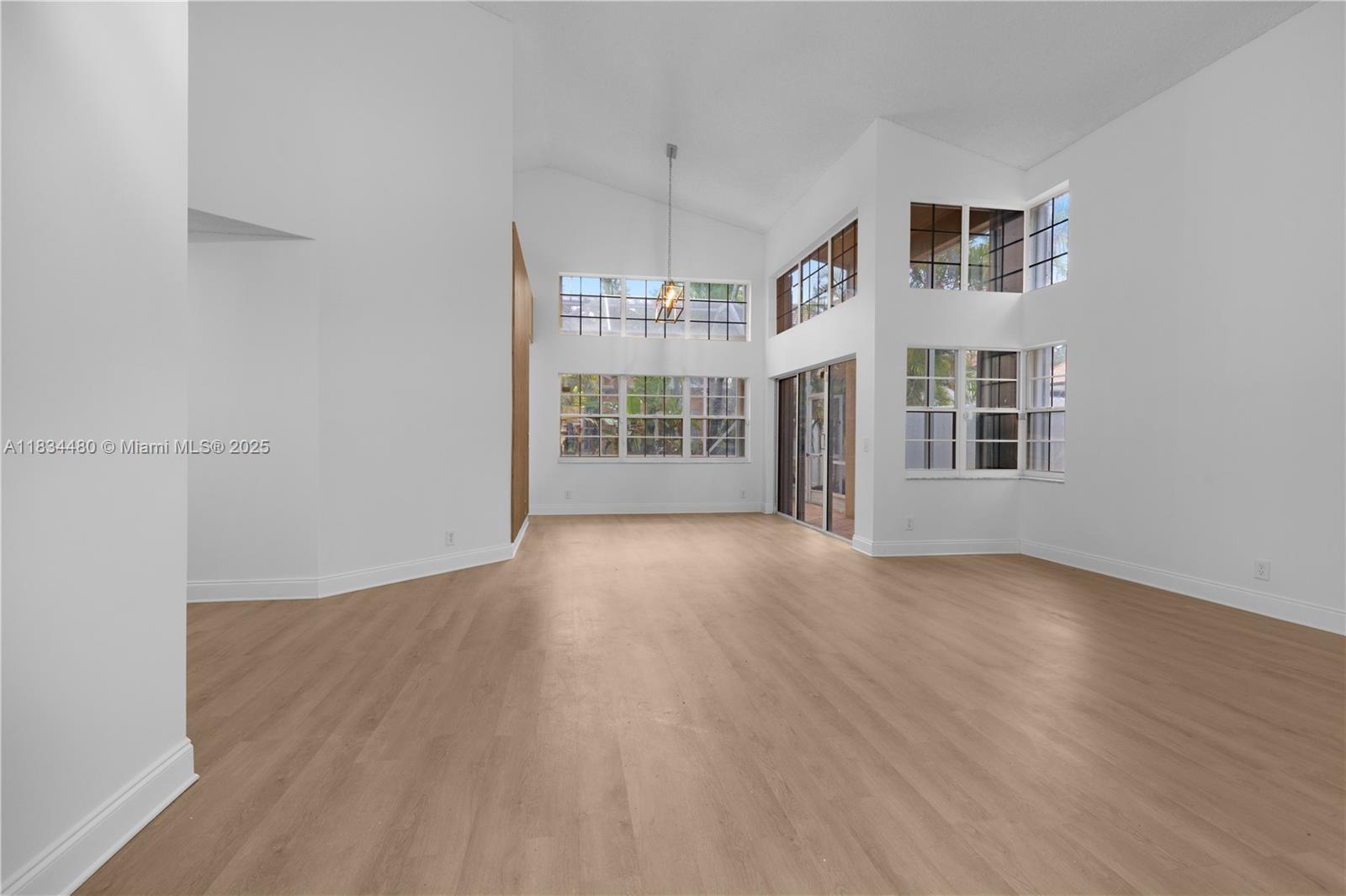 A spacious, empty room features vaulted ceilings, light wood flooring, and large windows — 1525 Seabay Rd, Weston FL 33326, WESTON, FL