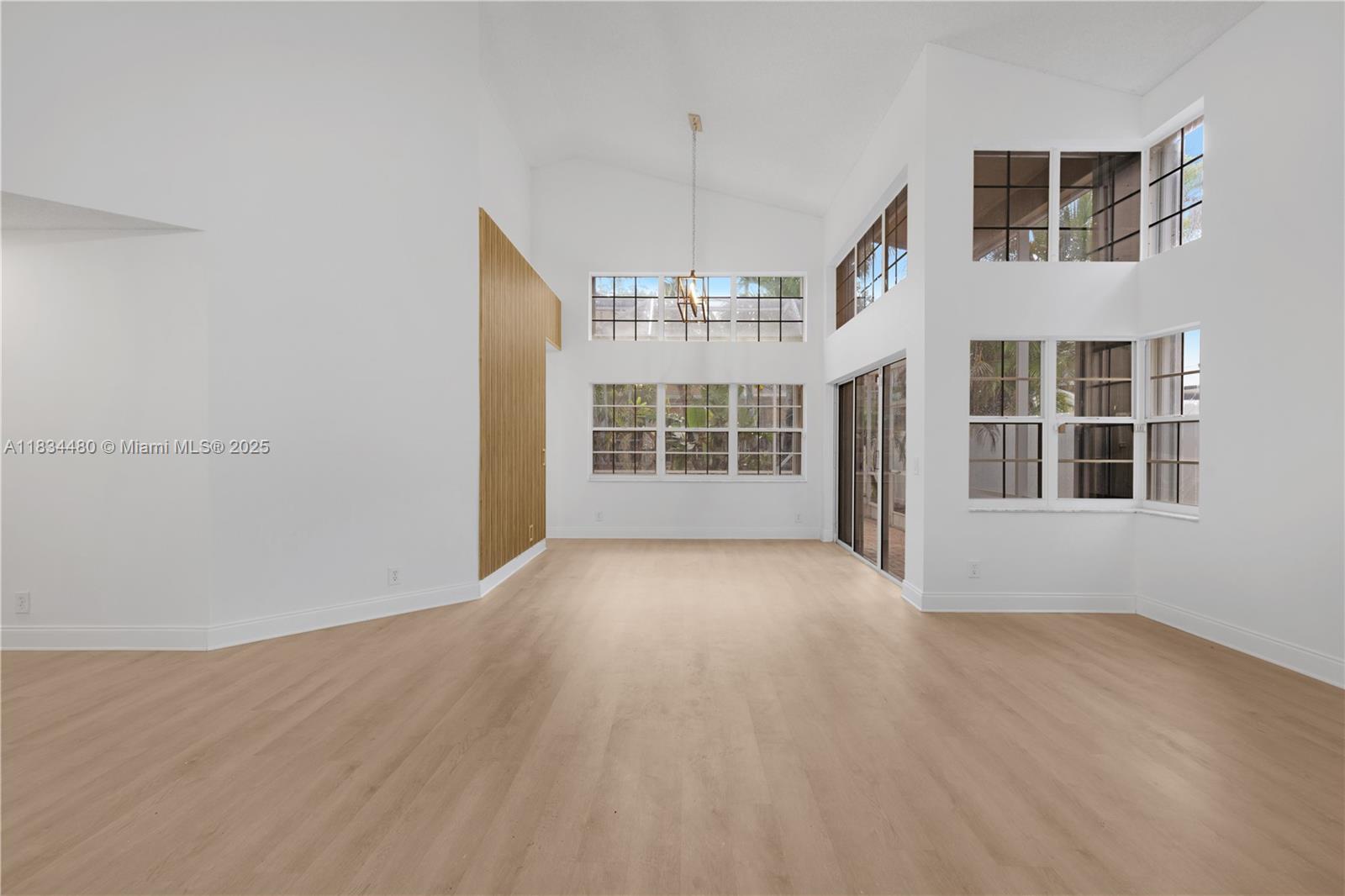 A bright, empty living room features high vaulted ceilings, light wood flooring, and large windows — 1525 Seabay Rd, Weston FL 33326, WESTON, FL