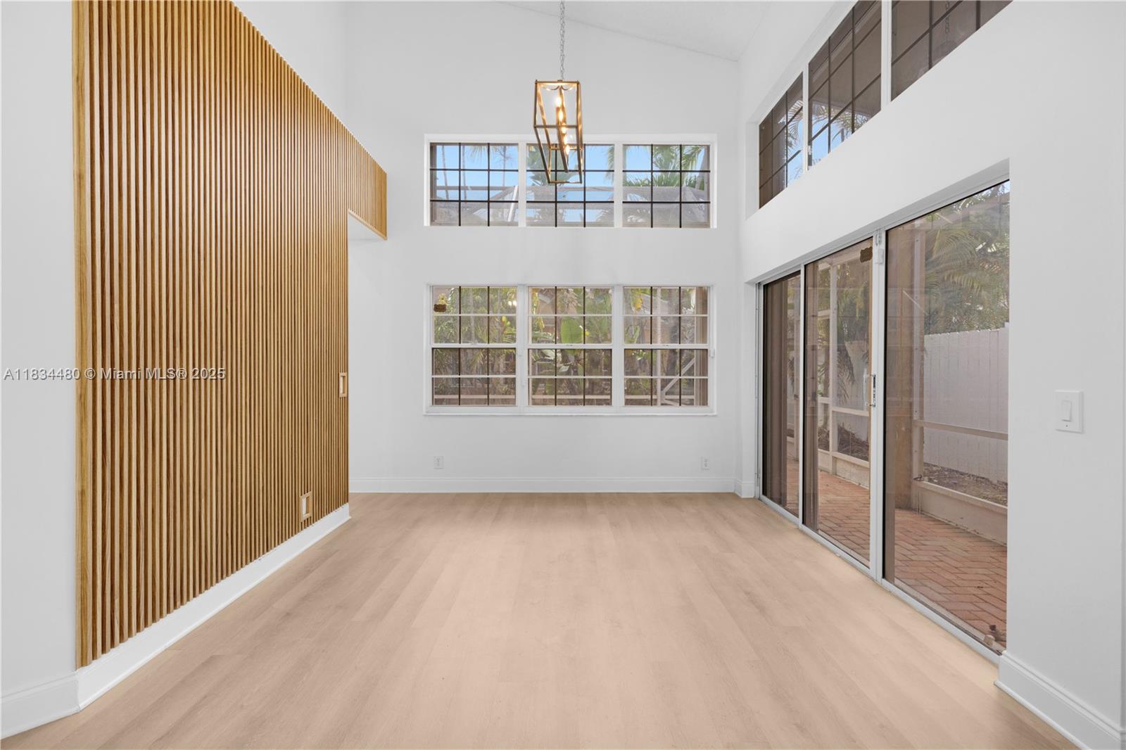 A bright room features light wood flooring, a slatted wood accent wall, and large windows — 1525 Seabay Rd, Weston FL 33326, WESTON, FL