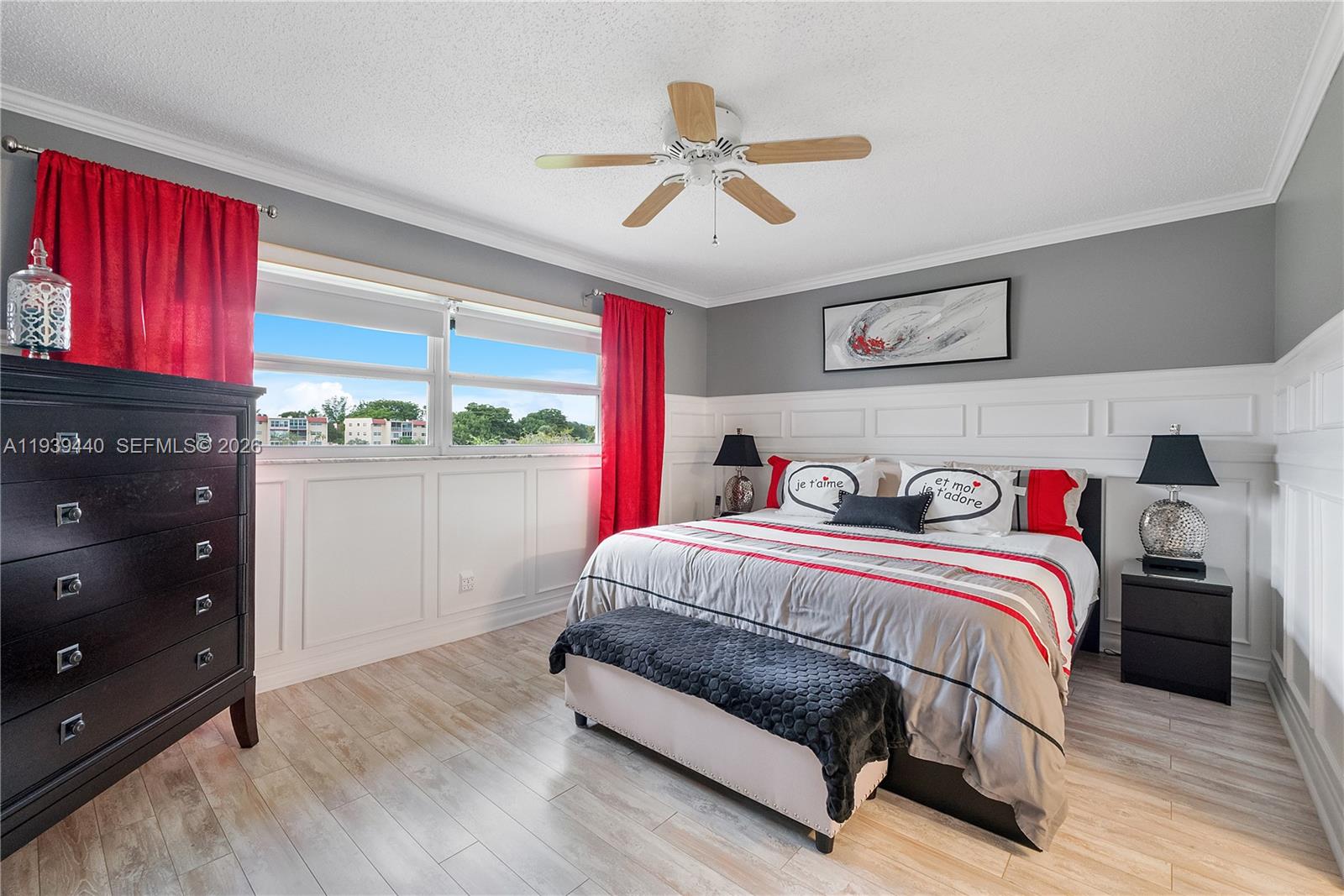 A bedroom features a bed with red and grey bedding, white wainscoting, and red curtains — 7847 Golf Circle Dr # 309, Margate FL 33063, MARGATE, FL