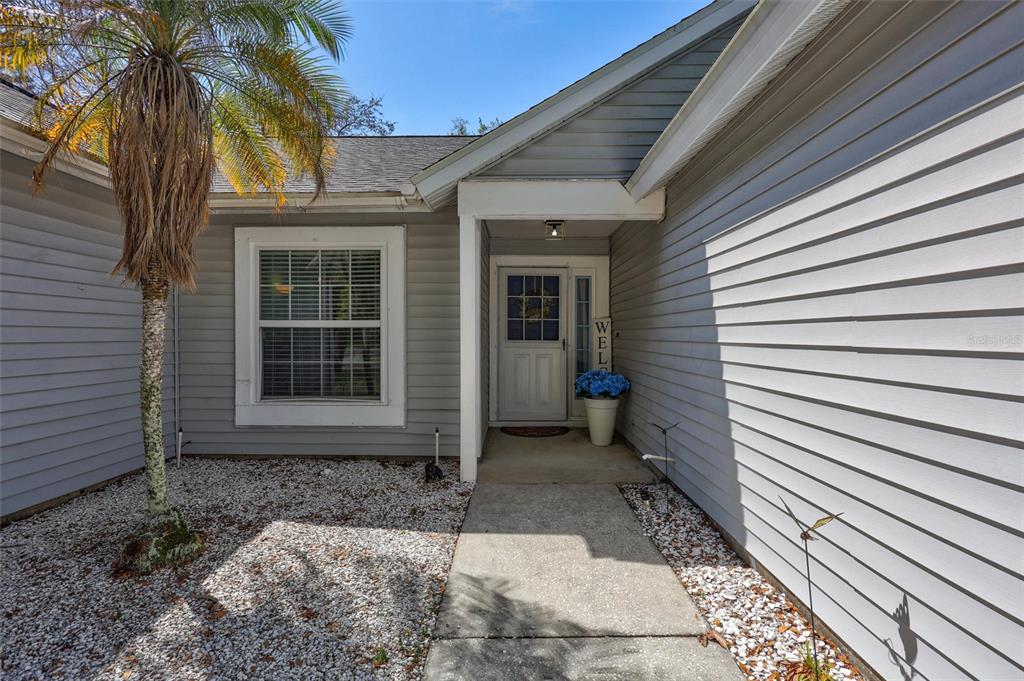 A gray-sided house exterior features a concrete walkway leading to a front door with sidelights — 1640 COUNTRYWOOD STREET, TARPON SPRINGS, FL