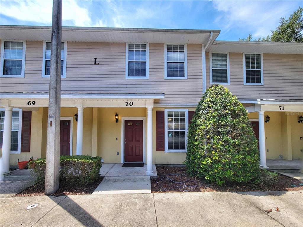 The exterior of a two-story townhouse building features beige siding, red doors, and white columns — 2508 SW 35TH PLACE UNIT 70, GAINESVILLE, FL