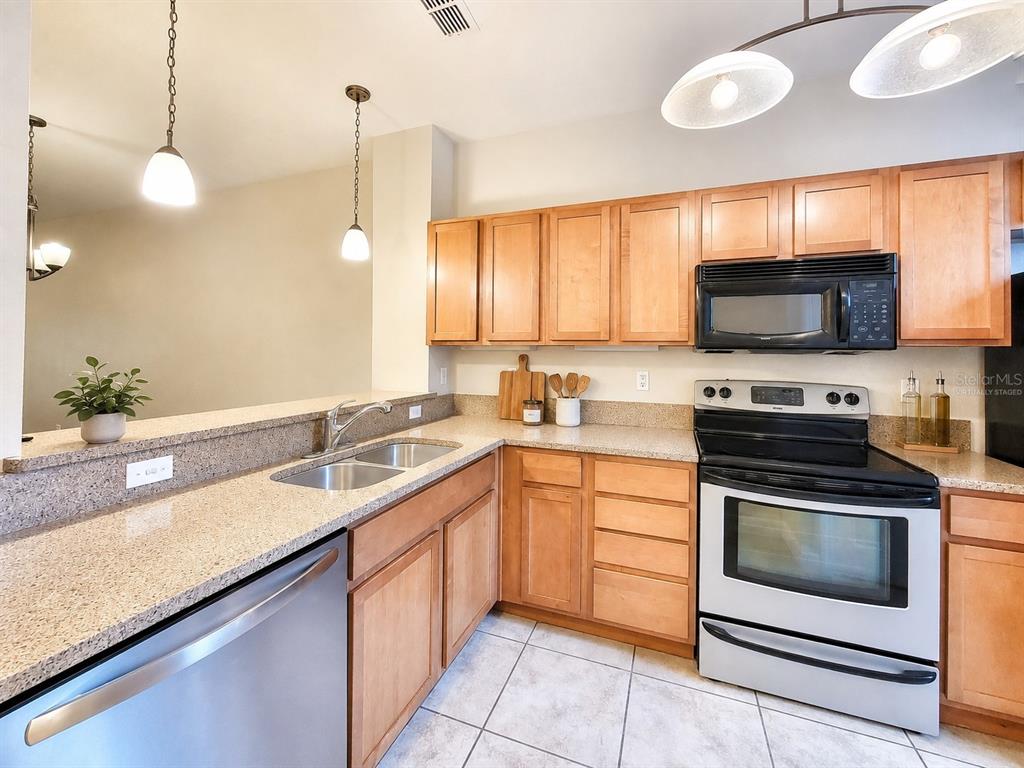 A kitchen features light wood cabinets, granite countertops, stainless steel appliances, and tile flooring — 2508 SW 35TH PLACE UNIT 70, GAINESVILLE, FL