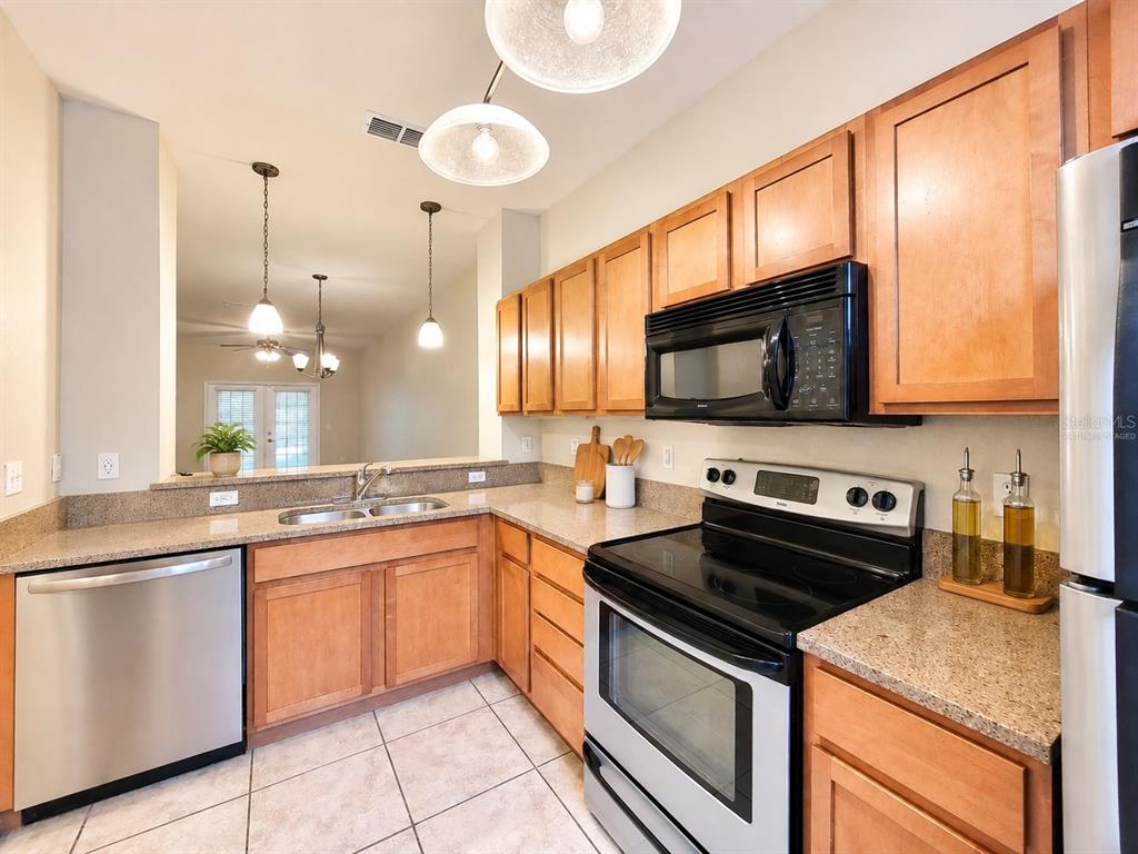 A kitchen features wood cabinets, stainless steel appliances, granite countertops, and tile flooring — 2508 SW 35TH PLACE UNIT 70, GAINESVILLE, FL