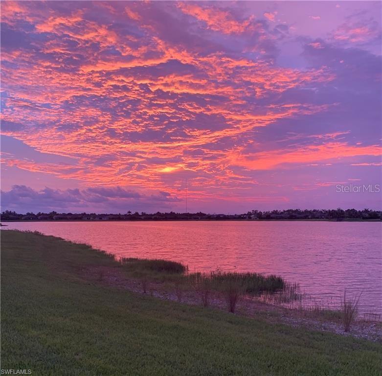 A vibrant sunset sky glows over a calm lake with grassy banks in the foreground — 16279 BONITA LANDING CIRCLE, BONITA SPRINGS, FL