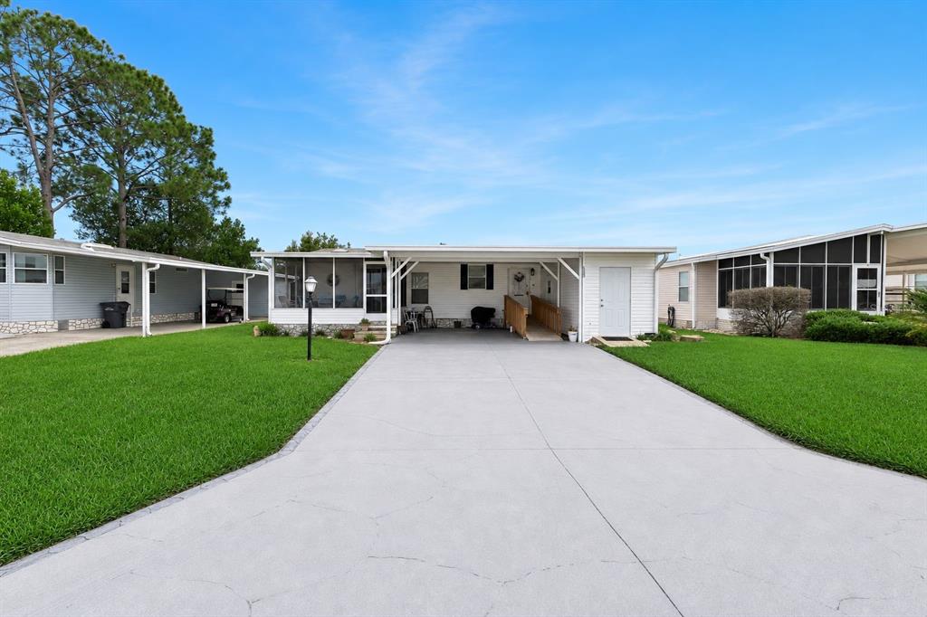 A white manufactured home features a concrete driveway, a carport, and a screened-in porch — 523 NESBITT PARK AVENUE, DAVENPORT, FL