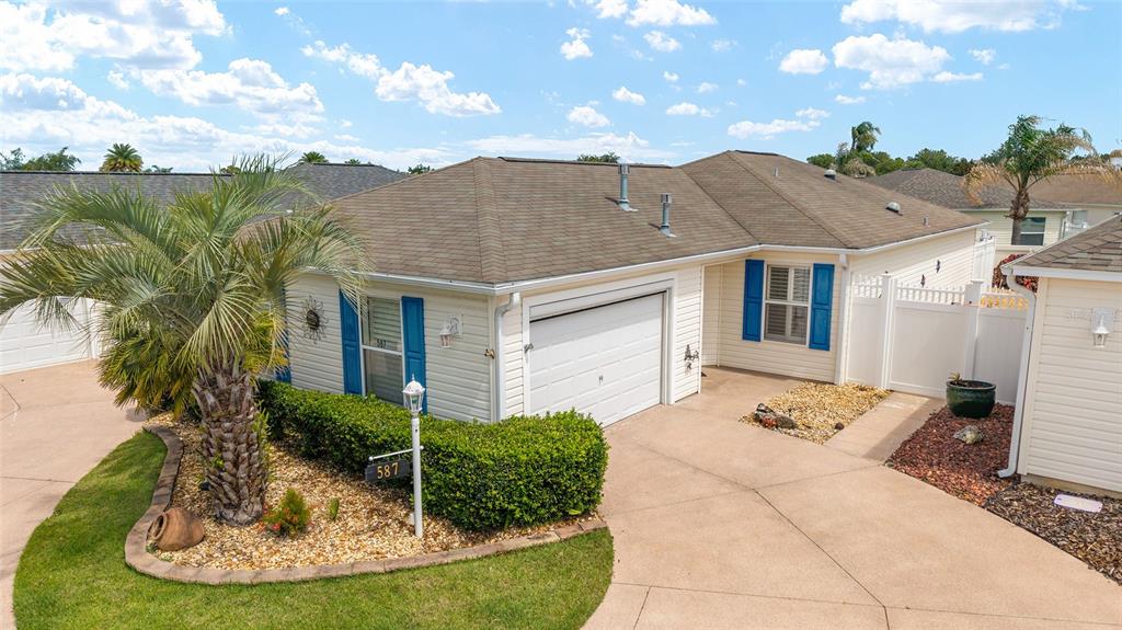 A single-story house with a white garage, blue shutters, and a palm tree in front — 587 AUDREY LANE, THE VILLAGES, FL