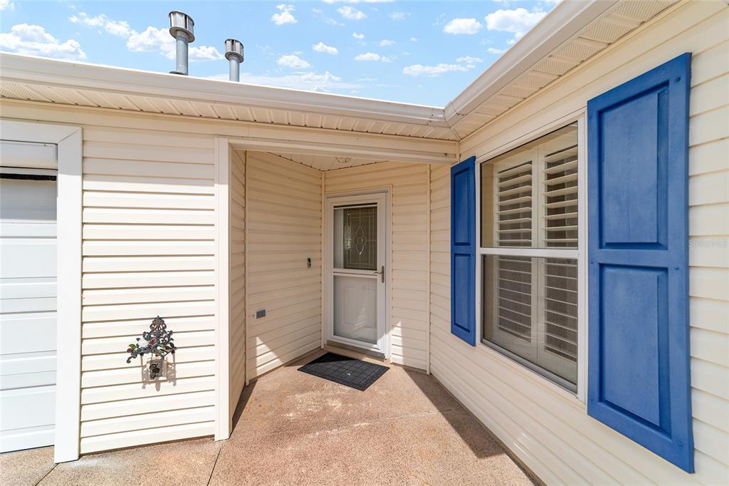 A beige vinyl-sided house exterior features a recessed front entrance and blue window shutters — 587 AUDREY LANE, THE VILLAGES, FL