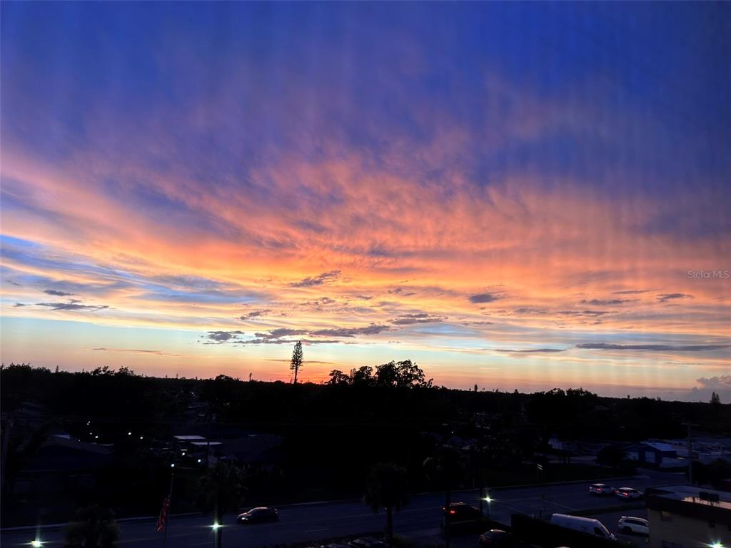 A vibrant sunset sky glows over a suburban landscape with trees and a road below — 2901 26TH STREET W UNIT 606, BRADENTON, FL