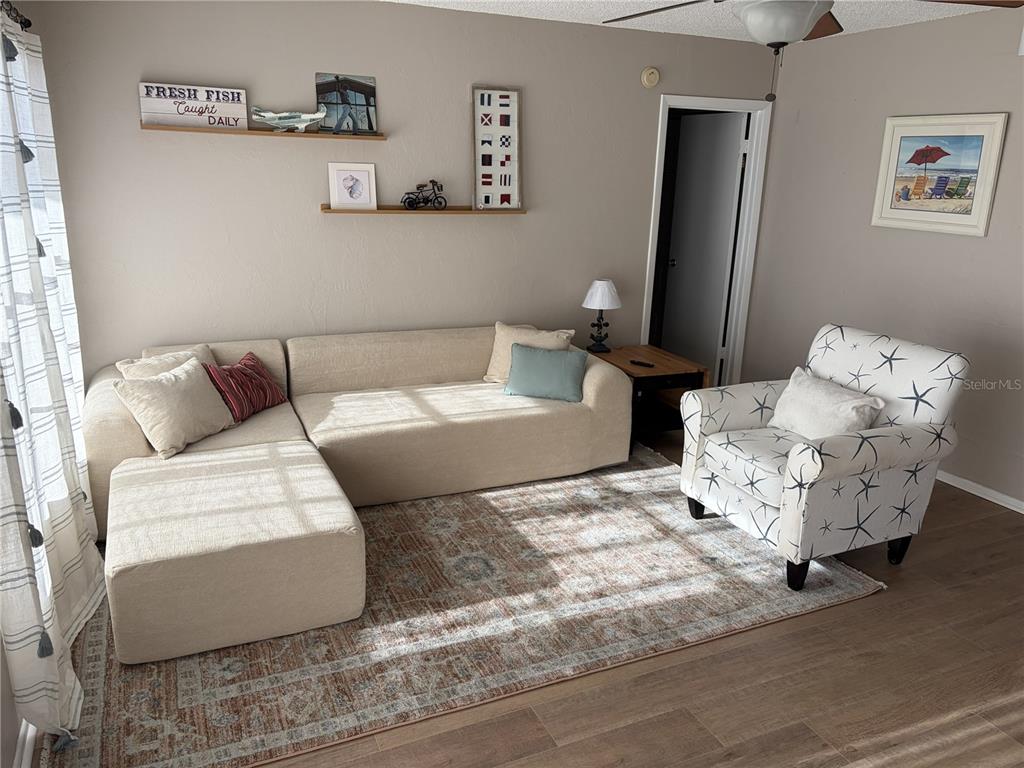 A living room features a beige sectional sofa, a patterned armchair, and wall-mounted shelves — 2901 26TH STREET W UNIT 606, BRADENTON, FL