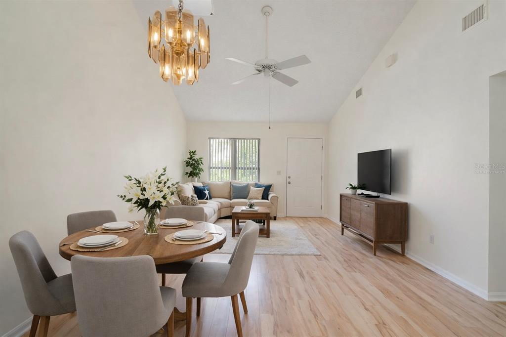 A living and dining area with light wood floors, a vaulted ceiling, and a chandelier — 397 ERON WAY UNIT 42, WINTER GARDEN, FL