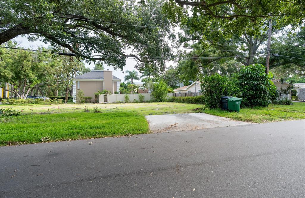 A vacant residential lot features a concrete driveway apron and mature trees under a cloudy sky — 2310 S HESPERIDES STREET, TAMPA, FL