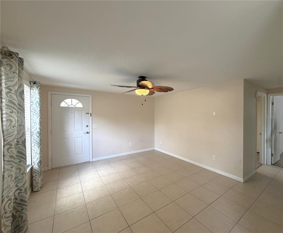 An empty room with beige walls, tile flooring, and a ceiling fan near an entrance — 634 DOGWOOD COURT, DUNEDIN, FL