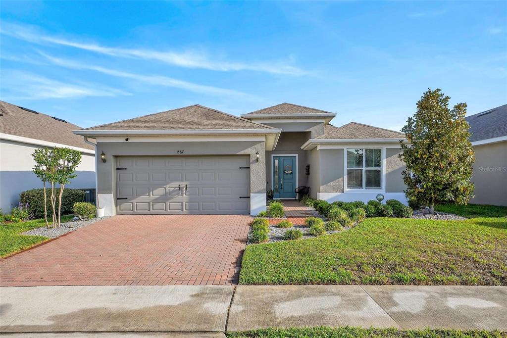 A single-story house with a gray stucco exterior, a brick driveway, and a blue door — 887 LADY BIRD LANE, ORANGE CITY, FL