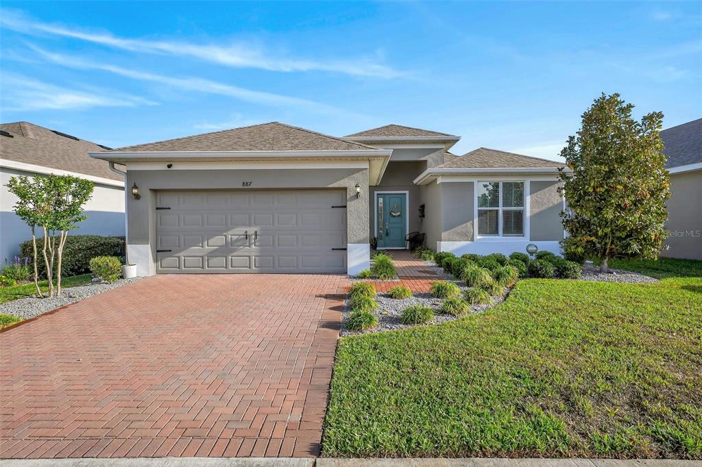 A single-story house with a brick paver driveway, a two-car garage, and a teal door — 887 LADY BIRD LANE, ORANGE CITY, FL