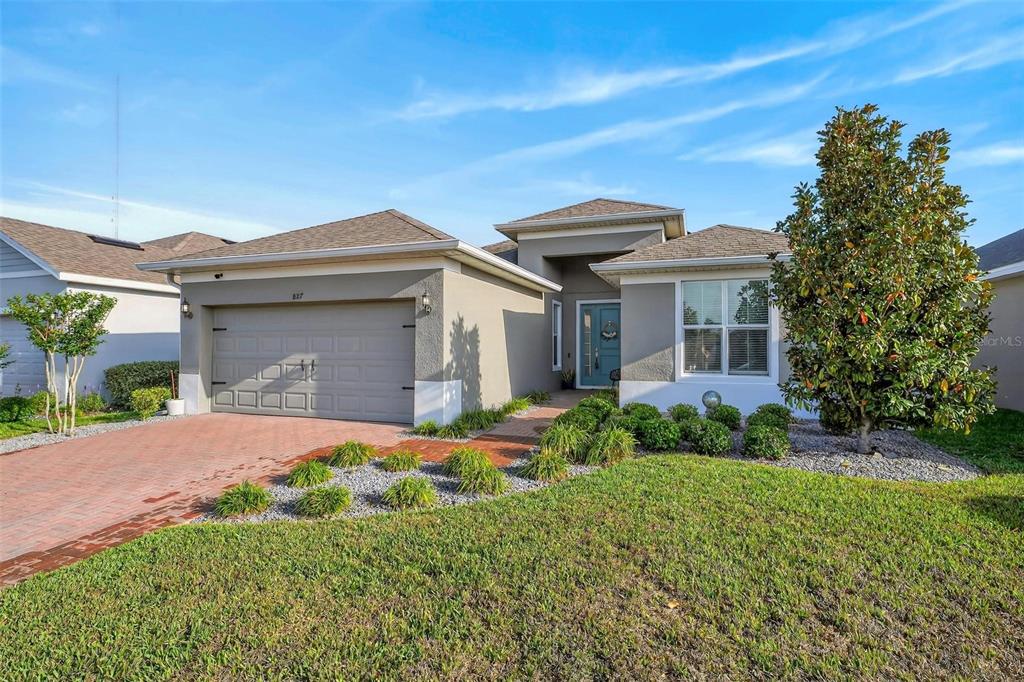 A single-story house with a gray stucco exterior, a two-car garage, and a brick driveway — 887 LADY BIRD LANE, ORANGE CITY, FL