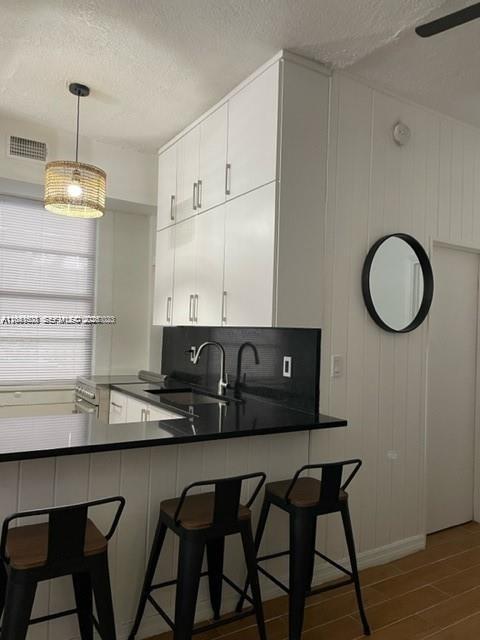 A kitchen features white cabinetry, a black countertop, and three black bar stools — 7149 Bay Dr # 2, Miami Beach FL 33141, MIAMI BEACH, FL