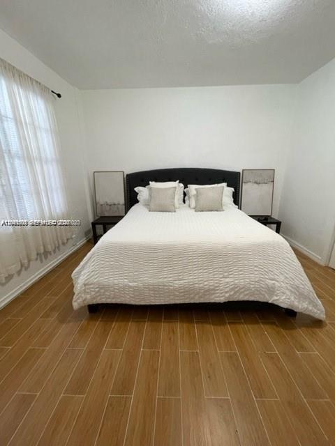 A bedroom features a bed with a dark headboard, white bedding, and wood-look tile flooring — 7149 Bay Dr # 2, Miami Beach FL 33141, MIAMI BEACH, FL